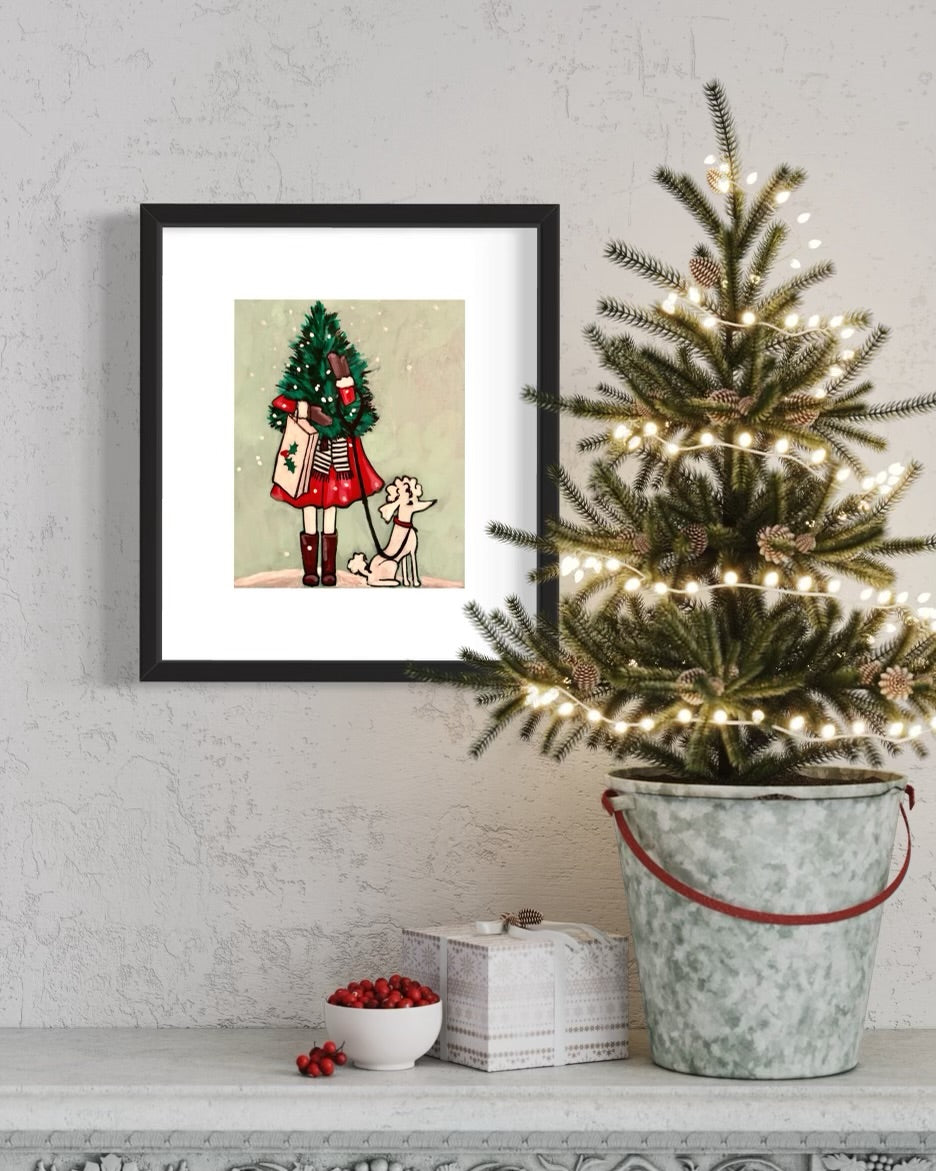 photo of framed Girl Holding Christmas Tree painting on wall with small Christmas tree and decorations on ledge in front of it