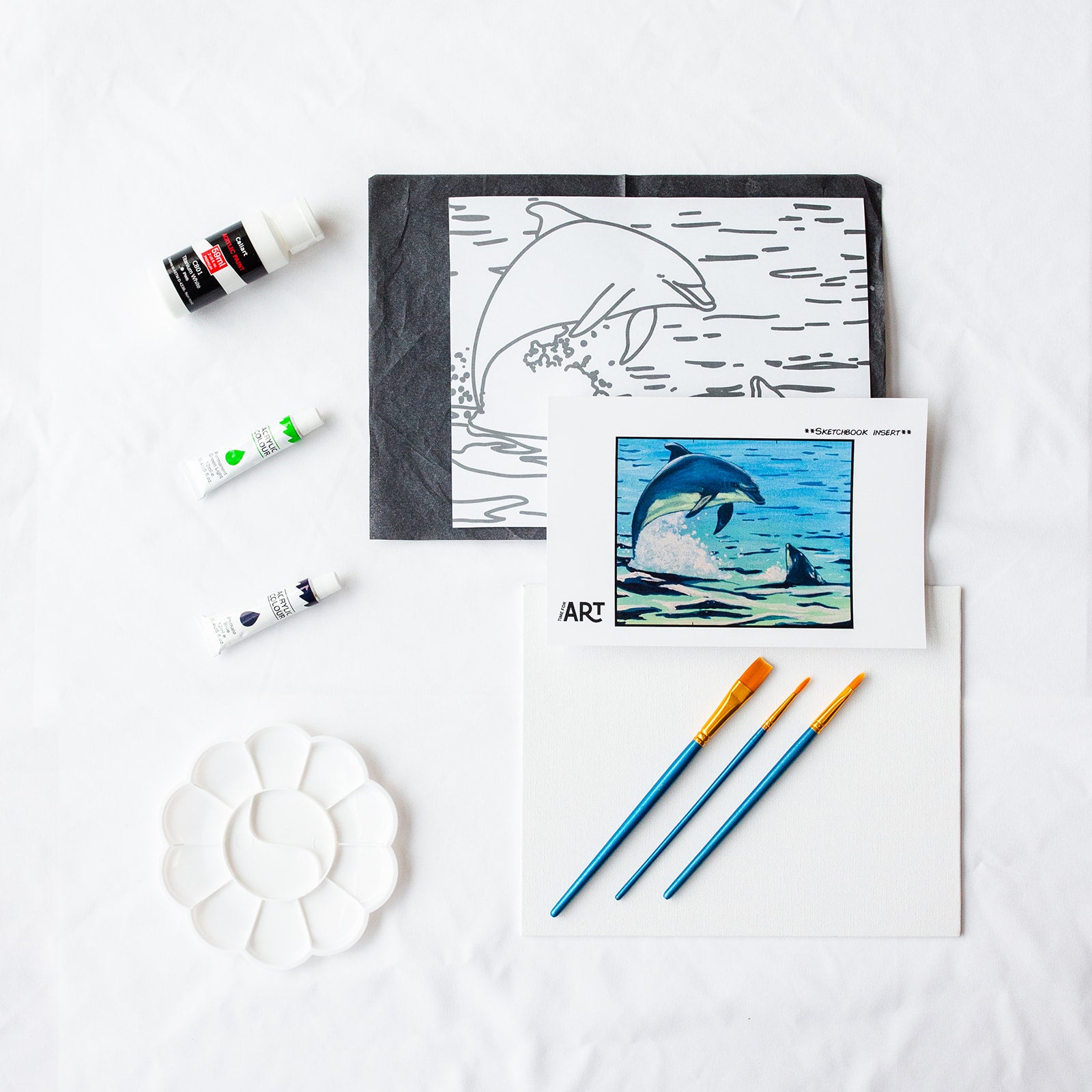 A picture of what is included in the Time For Art Playful Dolphins Painting Kit. The DIY Kit comes with 3 paints, a palette, the outline, brushes, canvas and more! 