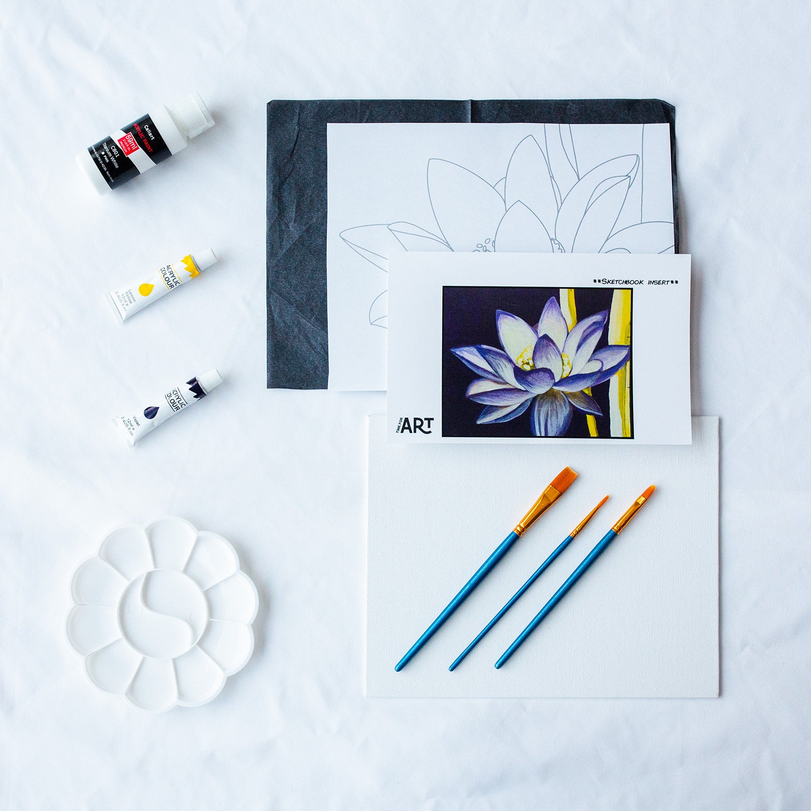 A picture of what is included in the Time For Art Purple Lotus Flower Painting Kit. The DIY Kit comes with 3 paints, a palette, the outline, brushes, canvas and more! 