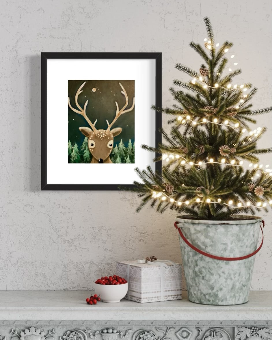 Christmas reindeer painting framed on wall with small Christmas tree and decorations in front